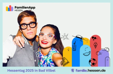 Ein junger Mann und eine Frau posieren lachend und Grimassen schneidend für ein Foto mit lustigen Brillen vor einem Hintergrund mit Figuren und Logos zum Hessentag.