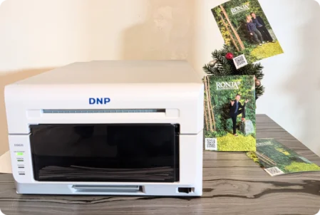 Ein kompakter weißer DNP DS620 Drucker steht auf einem Tisch. Daneben liegen ausgedruckte Fotos, die Ronja-Räubertochter-Szenen mit Schauspielern zeigen.