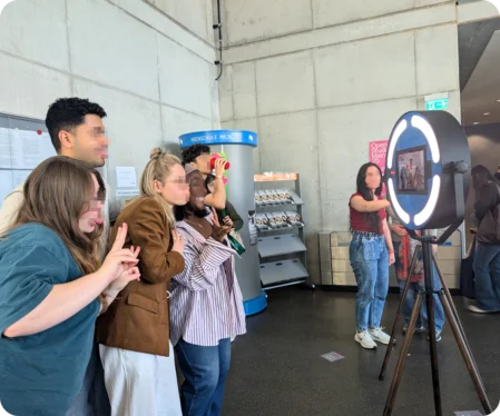 Eine Gruppe von Studenten posiert lachend und Grimassen schneidend vor einer Fotobox, die auf den Unternehmertagen der Hochschule Mainz steht.