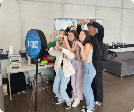 Eine Gruppe junger Erwachsener lacht und posiert für ein Foto vor einer blauen Fotobox mit dem Schriftzug „FOTOBOX“.