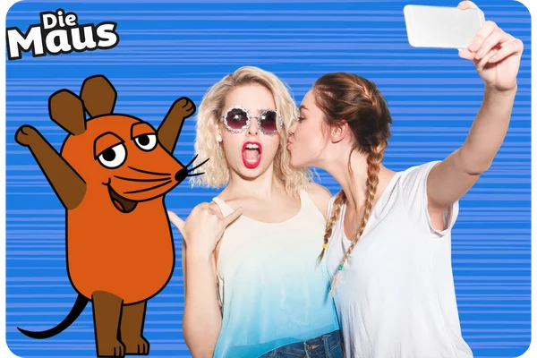 Zwei junge Frauen posieren lachend für ein Selfie. Eine der Frauen trägt eine Sonnenbrille und macht einen lustigen Ausdruck. Die Figur "Die Maus" ist als Fotobox-Overlay sichtbar.
