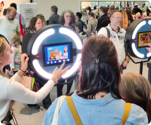Besucher stehen in einer Schlange, um Fotos an zwei Fotoboxen zu machen, die mit "Die Maus" Branding versehen sind. Auf den Bildschirmen sind beispielhafte Fotos mit den Charakteren zu sehen.