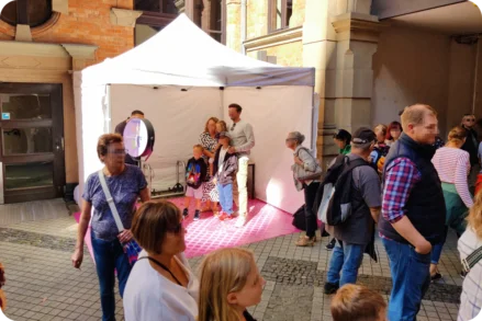 Eine Familie posiert für ein Foto in einer Fotobox, die unter einem weißen Zelt auf dem Stadtfest Wiesbaden am Rathaus aufgestellt ist. Im Vordergrund warten weitere Besucher in einer Schlange, um ebenfalls ein Foto zu machen.