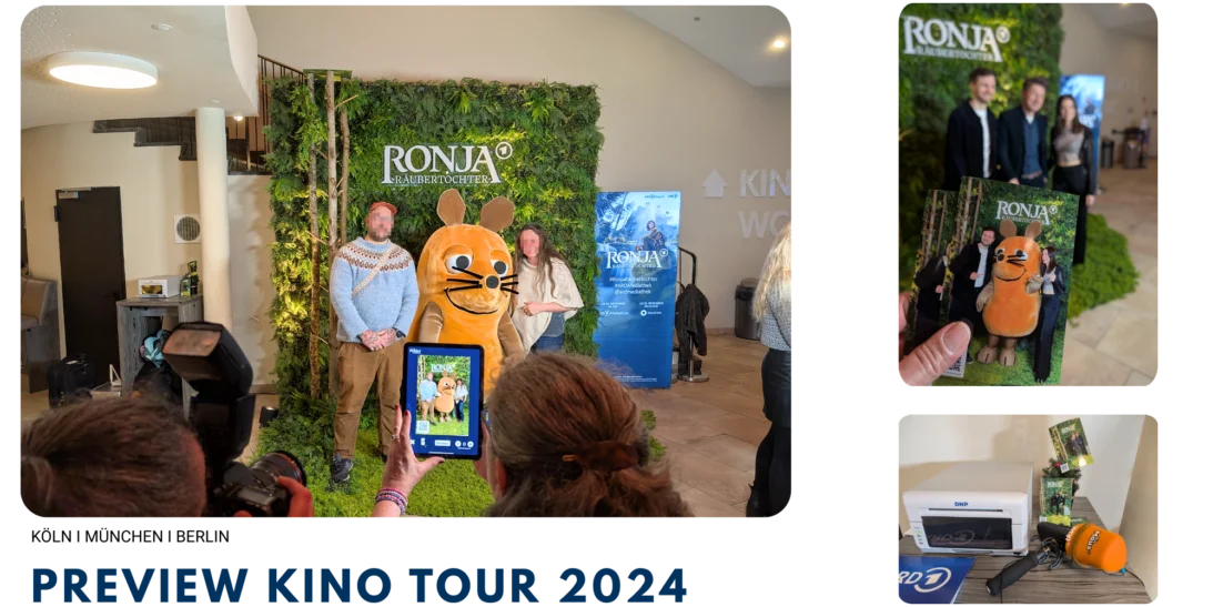 Besucher posieren auf der Kino-Preview von Ronja Räubertochter mit einem Walk Act in einem Biberkostüm. Ein Foto wird live auf dem Handy angezeigt und daneben steht ein Drucker zum Sofortausdruck.